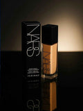 NARS Natural Radiant Longwear Foundation bottle and box, sleek black packaging, warm glow lighting