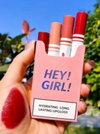 Pink lip gloss case with lipsticks and a swatch on a hand against a blurred natural background
